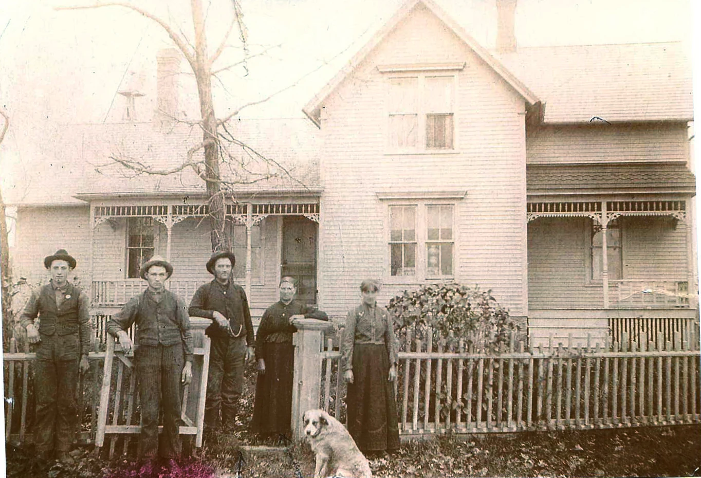 Victorian farmhouse with a family group of five adults and a dog posed at the porch fence